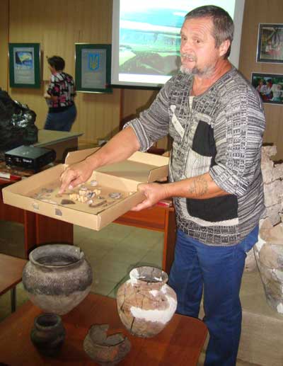 Эдуард Кравченко показывает находки Сидоровского археологического памятника. Перед ним на столике - сосуды, найденные в курганах Попов Яра.