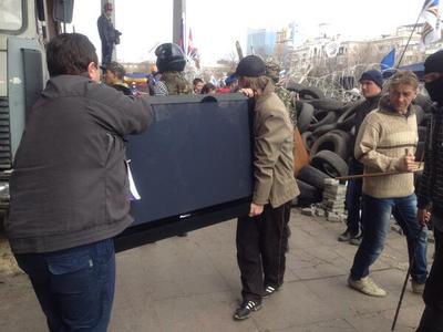 Активисты выносят из захваченного здания плазменный телевизор.